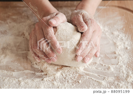Close-up of unrecognizable woman touching dough ball on board with flour while kneading 88095199