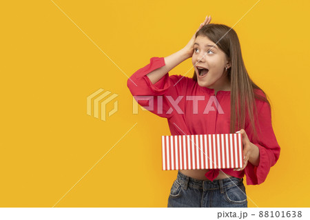 Surprised and overwhelmed girl with gift box in her hands on yellow background. Unexpected gift. 88101638