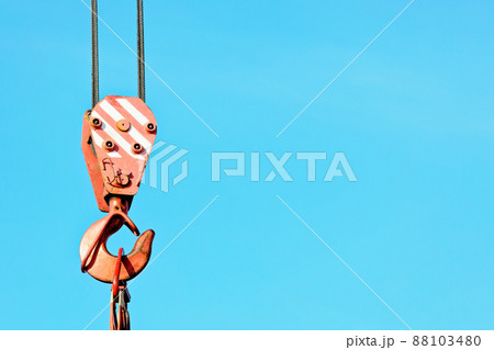 Crane hook with metal cable against blue sky. Unloading or loading of goods. Background with space Crane hook with metal cable against blue sky. Unloading or loading of goods. Background with space 88103480