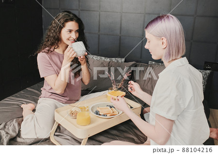 Happy young Caucasian lesbian women sitting at tray and having breakfast in bed 88104216