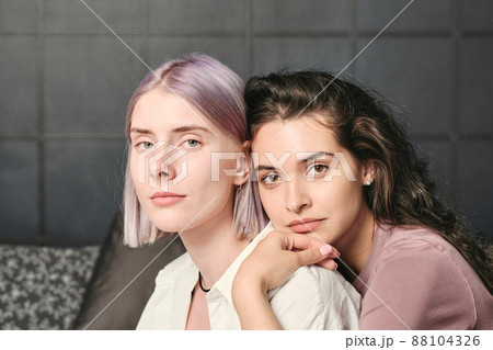 Calm young brown-haired woman leaning on shoulder of girlfriend while embracing her from back in bedroom Calm young brown-haired woman leaning on shoulder of girlfriend while embracing her from back in bedroom 88104326