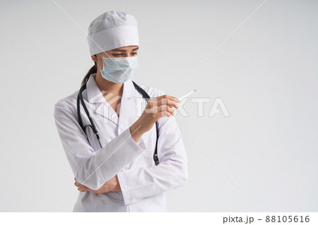 Doctor wearing face mask looking at measurement on medical thermometer over white background Doctor wearing face mask looking at measurement on medical thermometer over white background 88105616