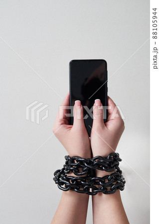 Iron chain that ties together hand and smartphone in concept of social media and internet addiction on gray background 88105944