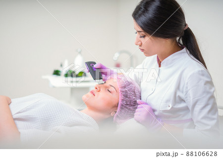 Hands of cosmetologist making ultrasound facial cleaning with special machine 88106628