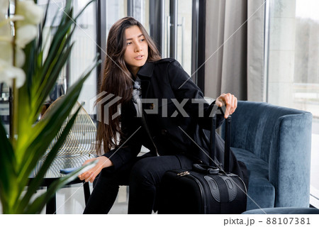 Woman sitting with suitcase in hotel lobby or in an airport lounge Woman sitting with suitcase in hotel lobby or in an airport lounge 88107381
