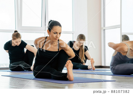 Group Of young women doing Yoga Exercises At Studio, making stretching poses in class indoors Group Of young women doing Yoga Exercises At Studio, making stretching poses in class indoors 88107382