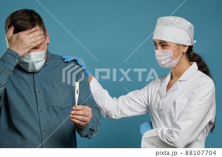 Young doctor measuring temperature of a patient with thermometer, studio shot on blue background 88107704