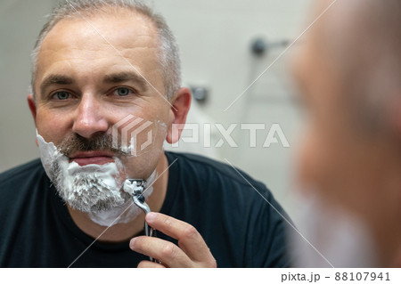 Middle aged handsome man shaving his beard in bathroom Middle aged handsome man shaving his beard in bathroom 88107941