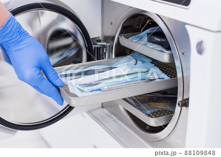 Assistant's hand in gloves insert packaged dental instrument to the autoclave to sterilise. Assistant's hand in gloves insert packaged dental instrument to the autoclave to sterilise. 88109848