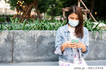 Portrait of a young woman in a medical mask for anti-coronavirus COVID-19 pandemic infectious disease outbreak protection and use a smartphone in Public area. Concept of Virus pandemic and pollution Portrait of a young woman in a medical mask for anti-coronavirus COVID-19 pandemic infectious disease outbreak protection and use a smartphone in Public area. Concept of Virus pandemic and pollution 88115648