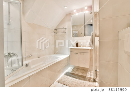 Bathroom with walls of flesh-colored tiles, bathtub, sink and mirrored wardrobe in a modern house Bathroom with walls of flesh-colored tiles, bathtub, sink and mirrored wardrobe in a modern house 88115990