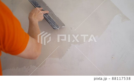 Hand with a spatula, work aligns wall. The solution is applied with a spatula to the wall. Hand with a spatula, work aligns wall. The solution is applied with a spatula to the wall. 88117538