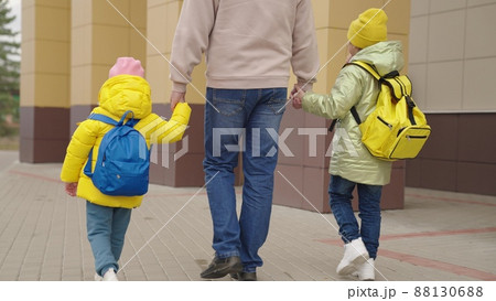 dad leads the girls' daughters by the hand to school, backpacks with books on shoulders of schoolgirls, hold older father by the hand, pick up little kid from school, education and upbringing lessons 88130688