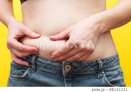 Woman hands compresses the fat on her belly on a yellow background. 88131221
