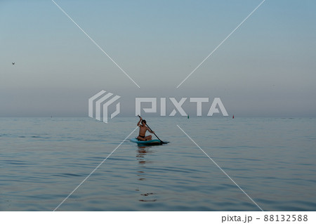 A boy of 11 years old swims on a SUP board in the sea after sunset. A boy of 11 years old swims on a SUP board in the sea after sunset. 88132588