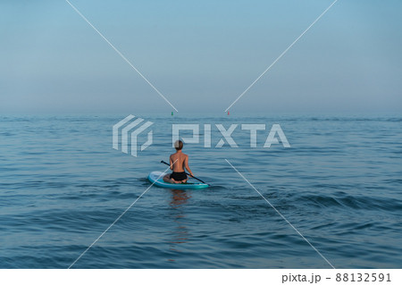A boy of 11 years old swims on a SUP board in the sea after sunset. 88132591