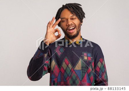 Extremely satisfied bearded african man with dreadlocks showing ok sign with self-confident facial expression, everything is fine, approval. Indoor studio shot isolated on gray background 88133145