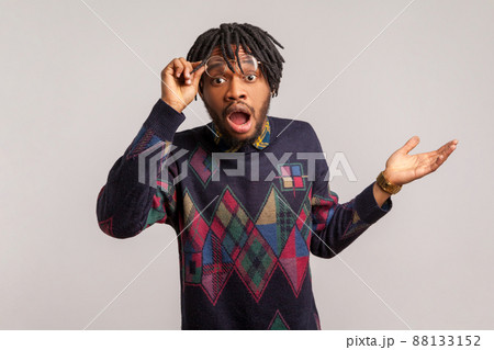 Extremely amazed and shocked african man with beard and dreadlocks looking at camera with widely opened eyes and mouth, surprised and confused with news. Indoor studio shot isolated on gray background 88133152