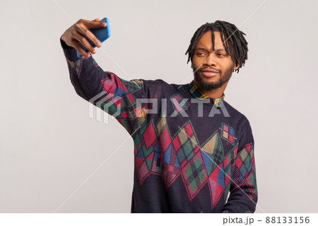 Funny african man with dreadlocks and beard holding smartphone in hand and posing at camera making selfie, camera application. Indoor studio shot isolated on gray background 88133156