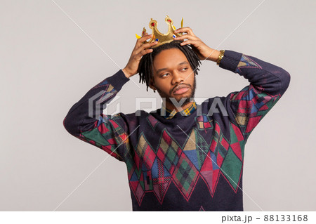 Egocentric self confident african man with dreadlocks trying on crown on his head, imagining himself king, leadership. Indoor studio shot isolated on gray background 88133168