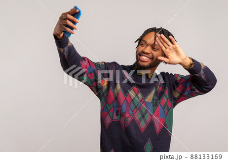 Happy cheerful african man in stylish sweatshirt with dreadlocks posing at camera with toothy smile, blogger saying hi to subscribers, live broadcast. Indoor studio shot isolated on gray background 88133169