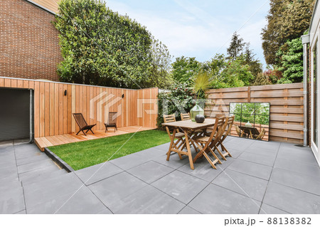 Stylish and well-maintained courtyard of the house with wooden table and chairs and a fresh lawn 88138382