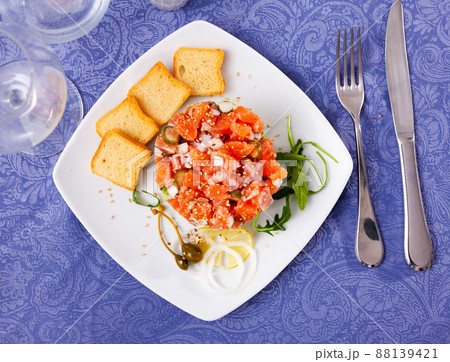 Salmon tartare with avocado served with toasts, greens, lemon and capers Salmon tartare with avocado served with toasts, greens, lemon and capers 88139421