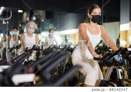 Young woman in mask with fitness bike in gym 88140247