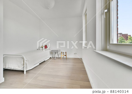 A small bedroom in a minimalist style with a simple bed and several windows 88140314