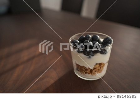 Granola with yogurt and blueberries in tumbler glass on walnut table Granola with yogurt and blueberries in tumbler glass on walnut table 88146585