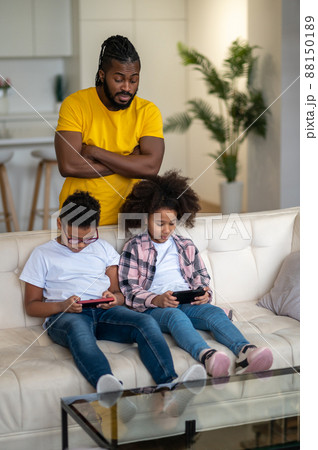 Dad watching children intently looking at smartphones Dad watching children intently looking at smartphones 88150189