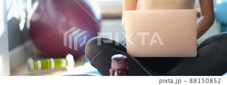 Woman sitting on floor with laptop, next to sports equipment Woman sitting on floor with laptop, next to sports equipment 88150852