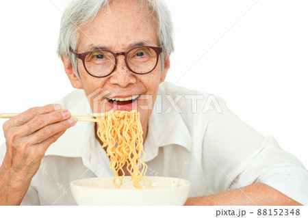 Beautiful happy old elderly people eating instant noodles with wooden chopsticks,Smiling asian senior woman eating delicious hot and spicy instant food,looking at camera,isolated on white background 88152348