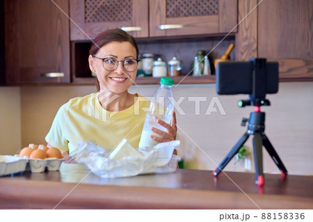 Woman cooking in kitchen talking online using video call on smartphone with tripod 88158336