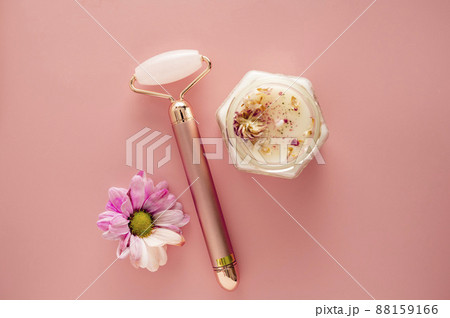 Pink quartz face roller with aroma candle and flower on grey background. Minimal beauty flatlay Pink quartz face roller with aroma candle and flower on grey background. Minimal beauty flatlay 88159166