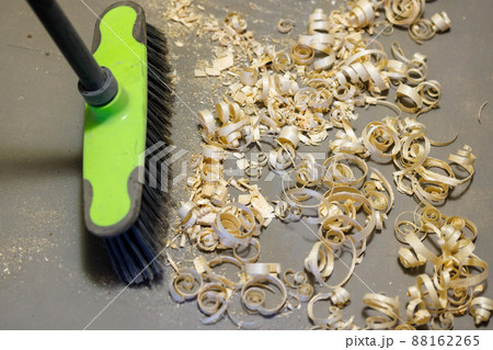 a small pile of wood shavings on a gray linoleum floor with a broom brush 88162265
