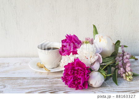 Summer coffee break; white cup of coffee and bunch of white and purple peonies flowers on white paint rustic wooden background; space for text Summer coffee break; white cup of coffee and bunch of white and purple peonies flowers on white paint rustic wooden background; space for text 88163327