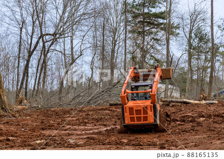 Excavator uprooting trees on land in bulldozer clearing land from trees, roots and branches Excavator uprooting trees on land in bulldozer clearing land from trees, roots and branches 88165135