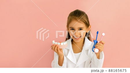 Doctor holds in his hands a model of the jaw and instruments for dental examination of the oral cavity. International Dentist's Day. Girl kid smiles sweetly shining with snow-white healthy teeth Doctor holds in his hands a model of the jaw and instruments for dental examination of the oral cavity. International Dentist's Day. Girl kid smiles sweetly shining with snow-white healthy teeth 88165675