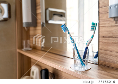 Two bright toothbrushes in glass cup in bathroom with mirror and window in hotel 88166016