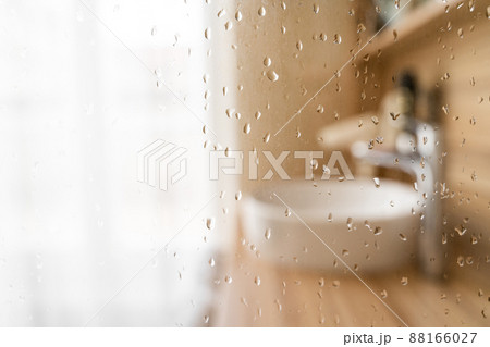 Wet glass shower door in hotel bathroom with blured window, sink and faucet 88166027