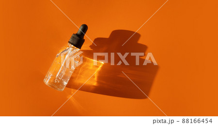 Transparent glass dropper bottle with air bubbles on orange background in sunlight. Pipette with fluid hyaluronic acid, serum, retinol. Cosmetics and healthcare concept Flat lay. Luxury beauty product Transparent glass dropper bottle with air bubbles on orange background in sunlight. Pipette with fluid hyaluronic acid, serum, retinol. Cosmetics and healthcare concept Flat lay. Luxury beauty product 88166454