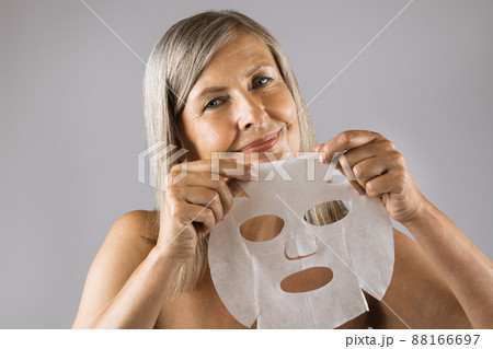Senior woman smiling on camera with cotton mask in hands 88166697
