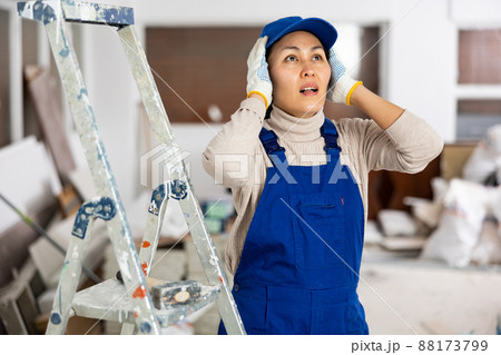 Frustrated woman builder holding head while standing in construction site Frustrated woman builder holding head while standing in construction site 88173799