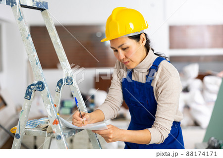 Woman worker filling documents during repair works indoors Woman worker filling documents during repair works indoors 88174171