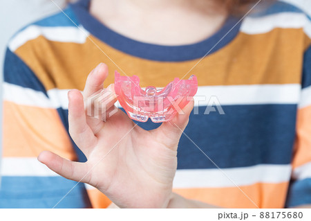 Cute little girl with blond hair is holding a pink dental myofunctional trainer 88175680