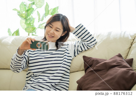 ソファに座りながらスマホ動画を見る30代女性 ソファに座りながらスマホ動画を見る30代女性 88176312