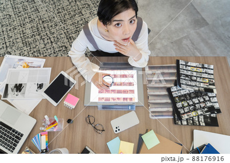 デスクでルーペで写真のネガを見る若い女性ファッションエディター デスクでルーペで写真のネガを見る若い女性ファッションエディター 88176916