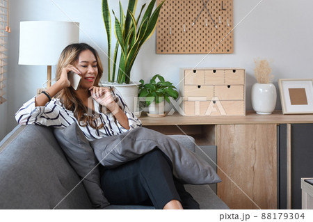 Beautiful millennial woman resting on couch at home and talking on mobile phone. 88179304