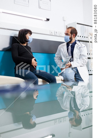Doctor showing human skeleton on tablet to pregnant adult at appointment during pandemic. Patient with pregnancy belly and physician talking about osteopathy scan in medical cabinet. Doctor showing human skeleton on tablet to pregnant adult at appointment during pandemic. Patient with pregnancy belly and physician talking about osteopathy scan in medical cabinet. 88183080